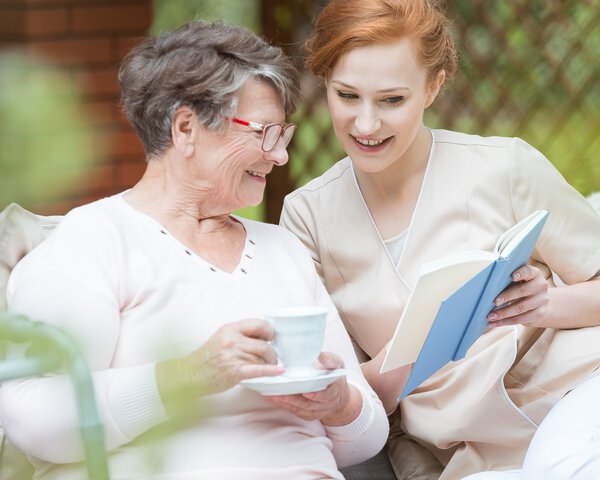 Eine junge Betreuerin zeigt einer älteren Dame etwas in einem Buch | © shutterstock_698351416